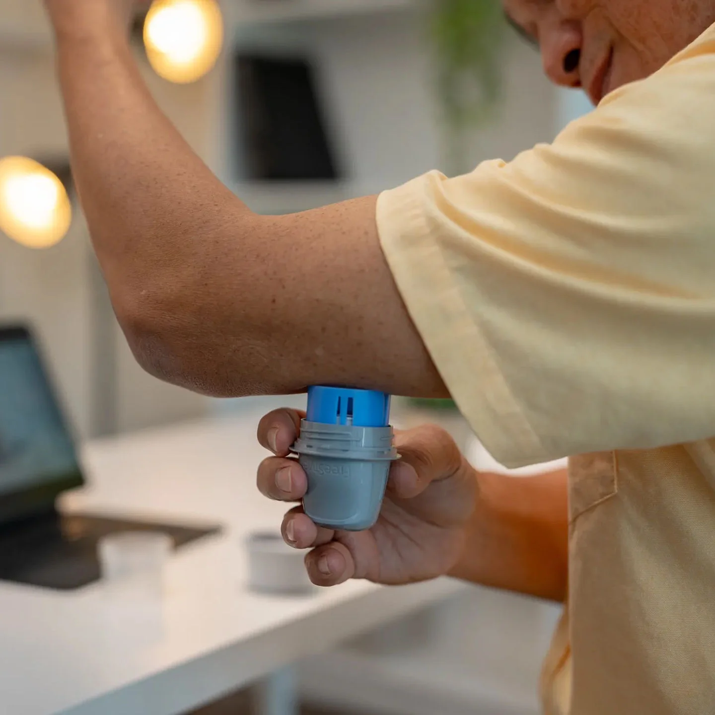 Person applying a FreeStyle Libre sensor to the back of their upper arm using the sensor applicator.