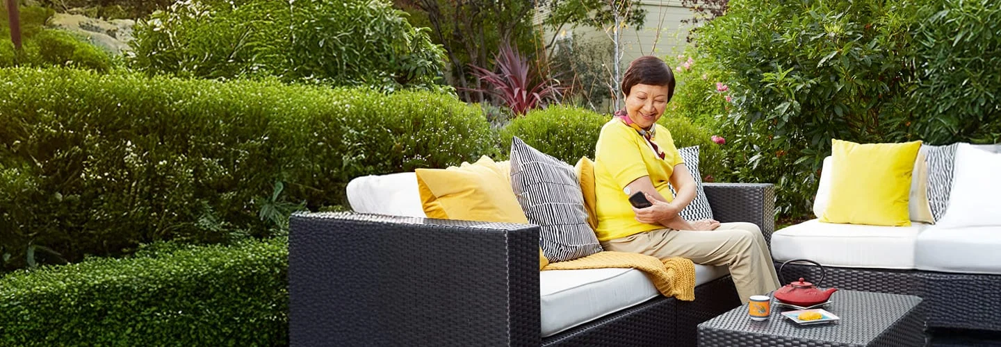 A man sitting on a deck wearing a FreeStyle Libre sensor looking at his phone.
