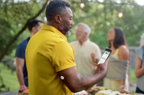 Man checking his smartphone outdoors while wearing a FreeStyle Libre 3 Plus sensor