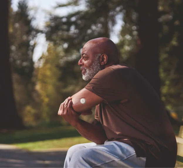 Hombre relajándose en un espacio natural después de ejercitarse, usando el sensor FreeStyle Libre.