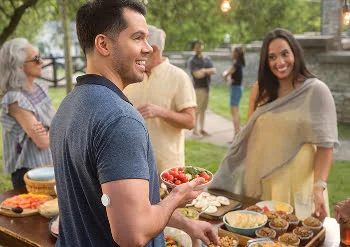 A man at an outdoor gathering holds a bowl of vegetables, with a FreeStyle Libre sensor on his upper arm.