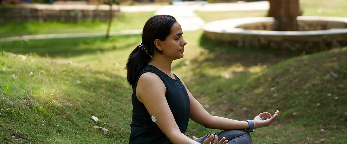 A woman kneeling on a yoga mat looking at glucose readings on her smartphone.