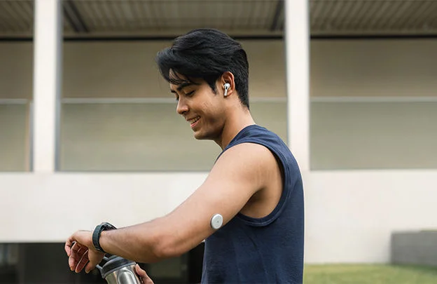 Homem olhando para um smartwatch e usando um sensor no braço.