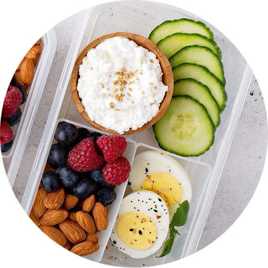 Snack box with cottage cheese, cucumber slices, berries, almonds, and hard-boiled eggs for balanced snacking.