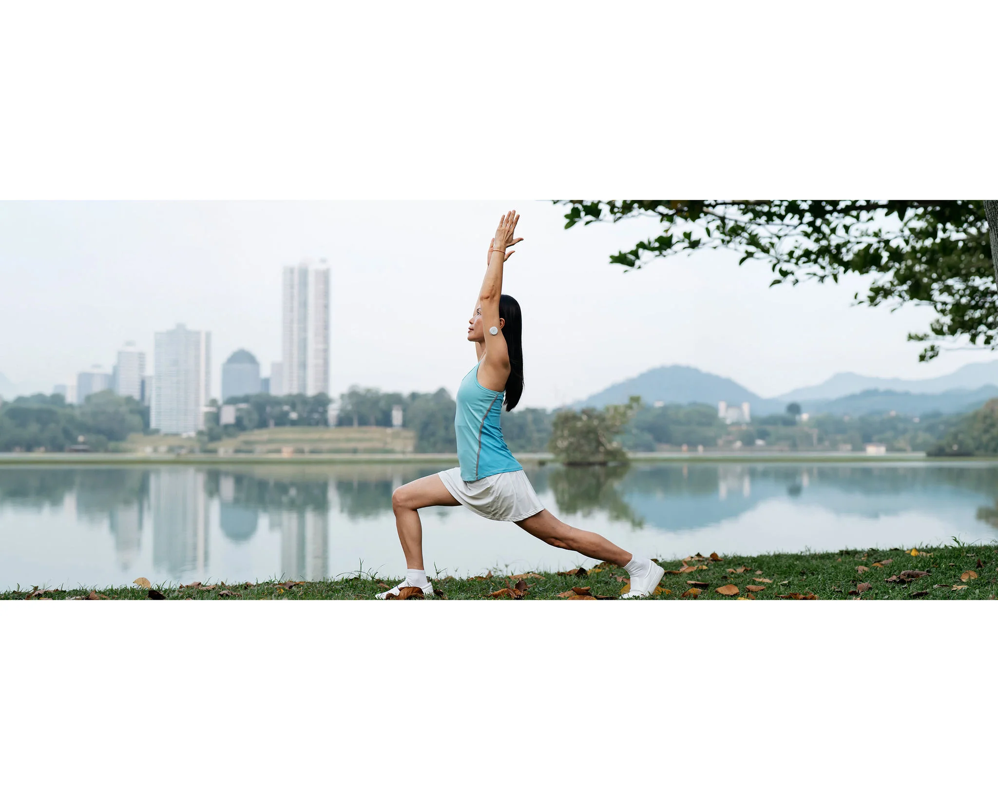 A women wearing a FreeStyle Libre sensor on the upper arm while exercising beside a lake with a city skyline in the background.