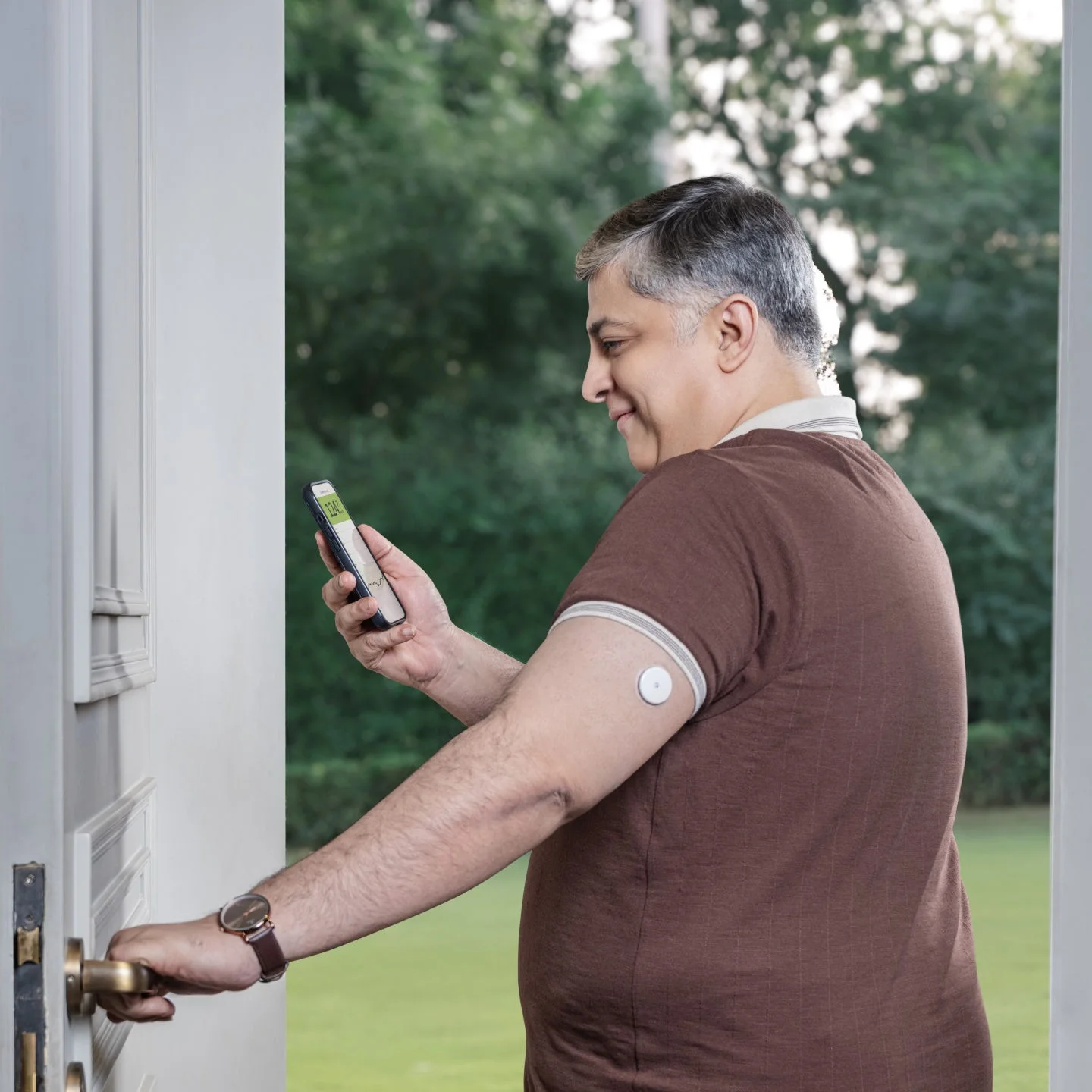 Man standing in the doorway of a house looking at his smartphone.