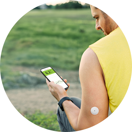 Man wearing a maroon shirt, with a FreeStyle Libre sensor on his arm, looking at a phone screen showing his glucose readings 