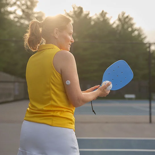 A woman wearing a Freestyle Libre sensor playing pickleball