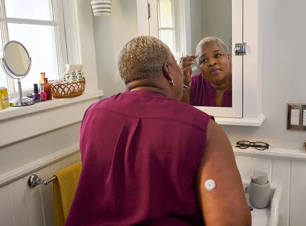 Mujer mirándose al espejo del baño mientras usa el sensor FreeStyle Libre en el brazo
