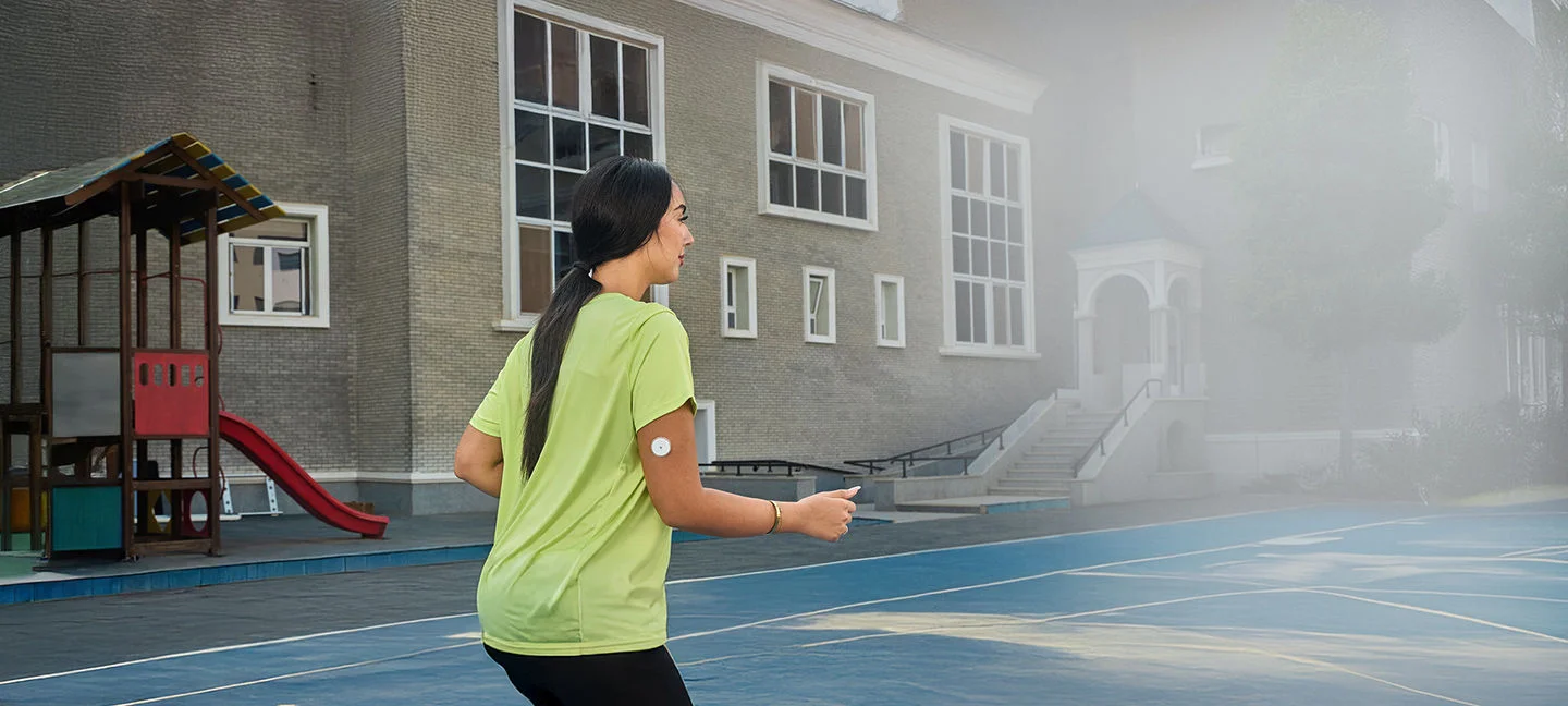 A woman wearing a Freestyle Libre sensor balancing on an exercise ball while smiling broadly.