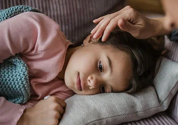Caregiver stroking the head of sick child lying down.