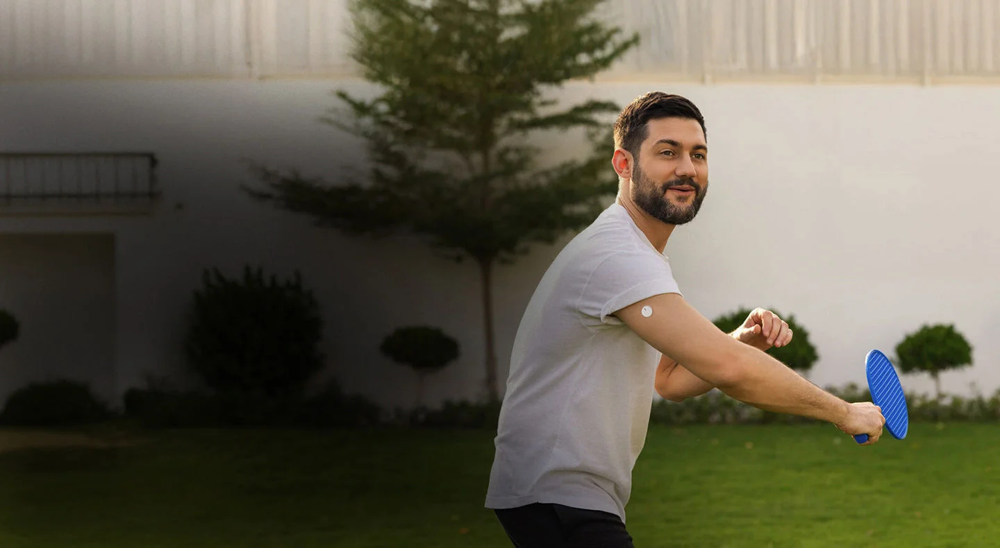 A man outdoors wearing a FreeStyle Libre sensor while playing raquet.
