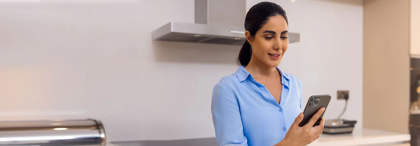 A woman standing in the kitchen while looking at his phone.