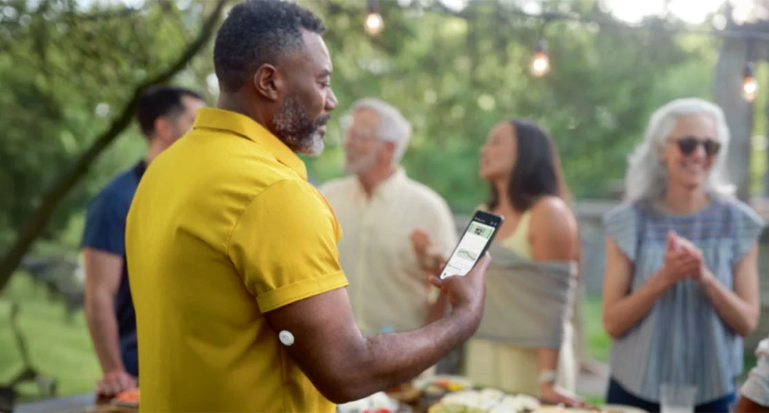 Man checking his smartphone outdoors while wearing a FreeStyle Libre 3 Plus sensor