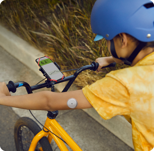 Dieťa so senzorom FreeStyle Libre 2 sediaci na bicykli so smartfónom prirobeným na riadidlách s otvorenou aplikáciou FreeStyle LibreLink.