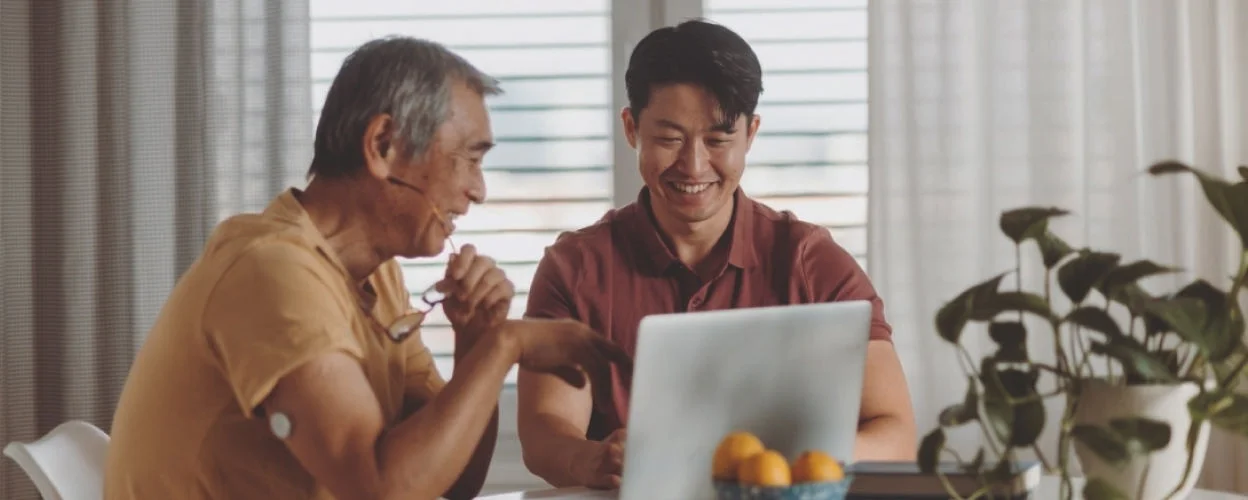 Two people using a laptop together at a table, with a FreeStyle Libre sensor visible on one upper arm, demonstrating connected diabetes management.