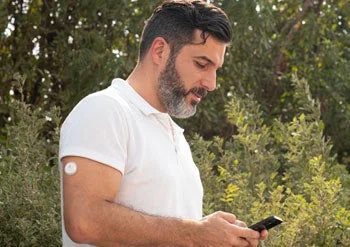 A man wearing a FreeStyle Libre sensor while looking at his phone.