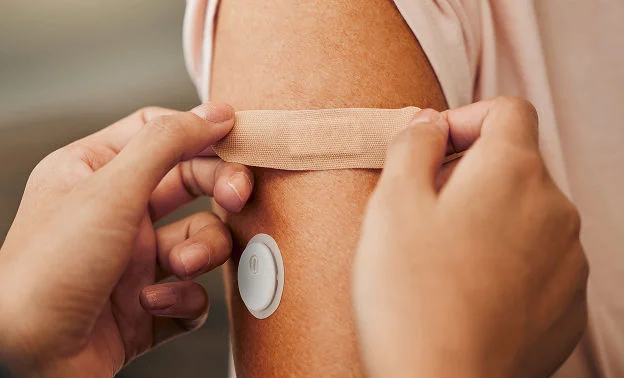 Der sættes et plaster på personens overarm tæt på FreeStyle Libre 3 Plus-sensoren