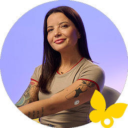 A person wearing a continuous glucose monitor (CGM) sits with arms crossed, showing tattoos on both arms.