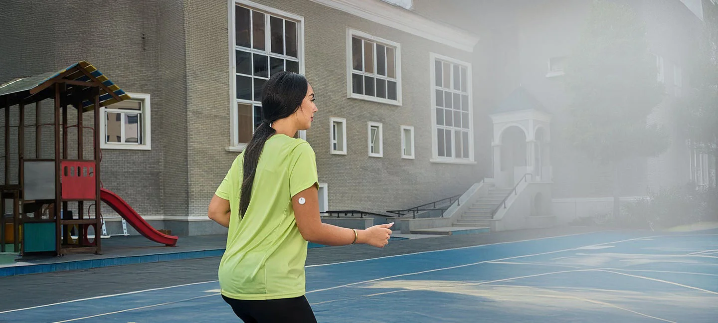 A woman wearing a Freestyle Libre sensor balancing on an exercise ball while smiling broadly.
