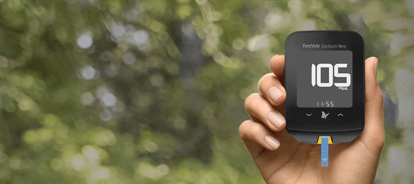 Mão segurando o medidor de glicose Optium Neo com a tela ligada