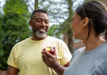 .A man chooses a healthy snack, enjoying a fresh apple while spending time outdoors with a companion.