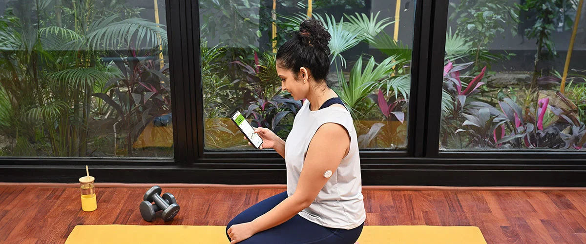 A woman wearing a Freestyle Libre sensor balancing on an exercise ball while smiling broadly.
