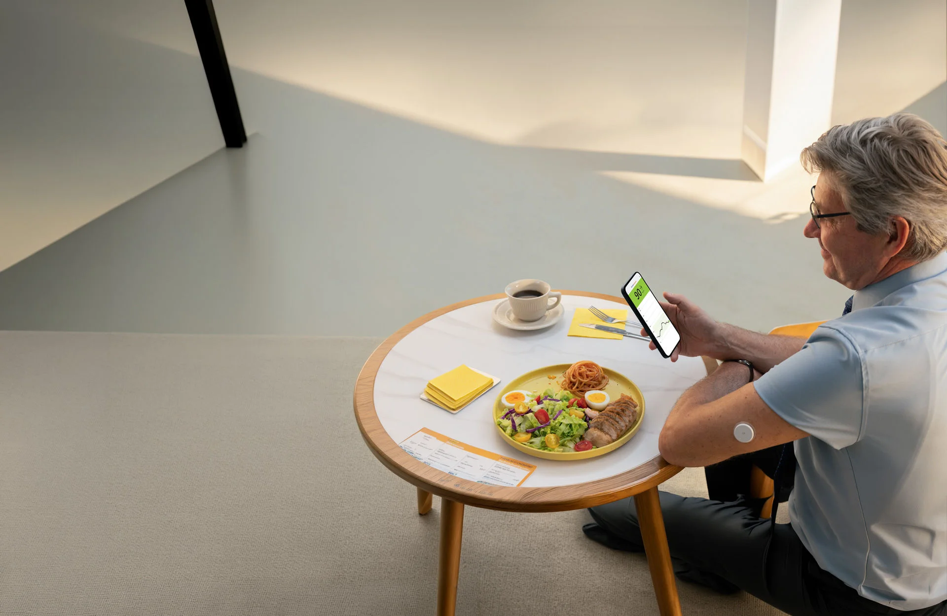 Persona sentada a una mesa con un plato de comida revisando una lectura de glucosa en un teléfono mientras usa un sensor FreeStyle Libre en el brazo