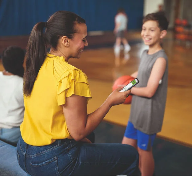 Mãe monitorando a glicose enquanto o filho, ao seu lado, segura uma bola de basquete