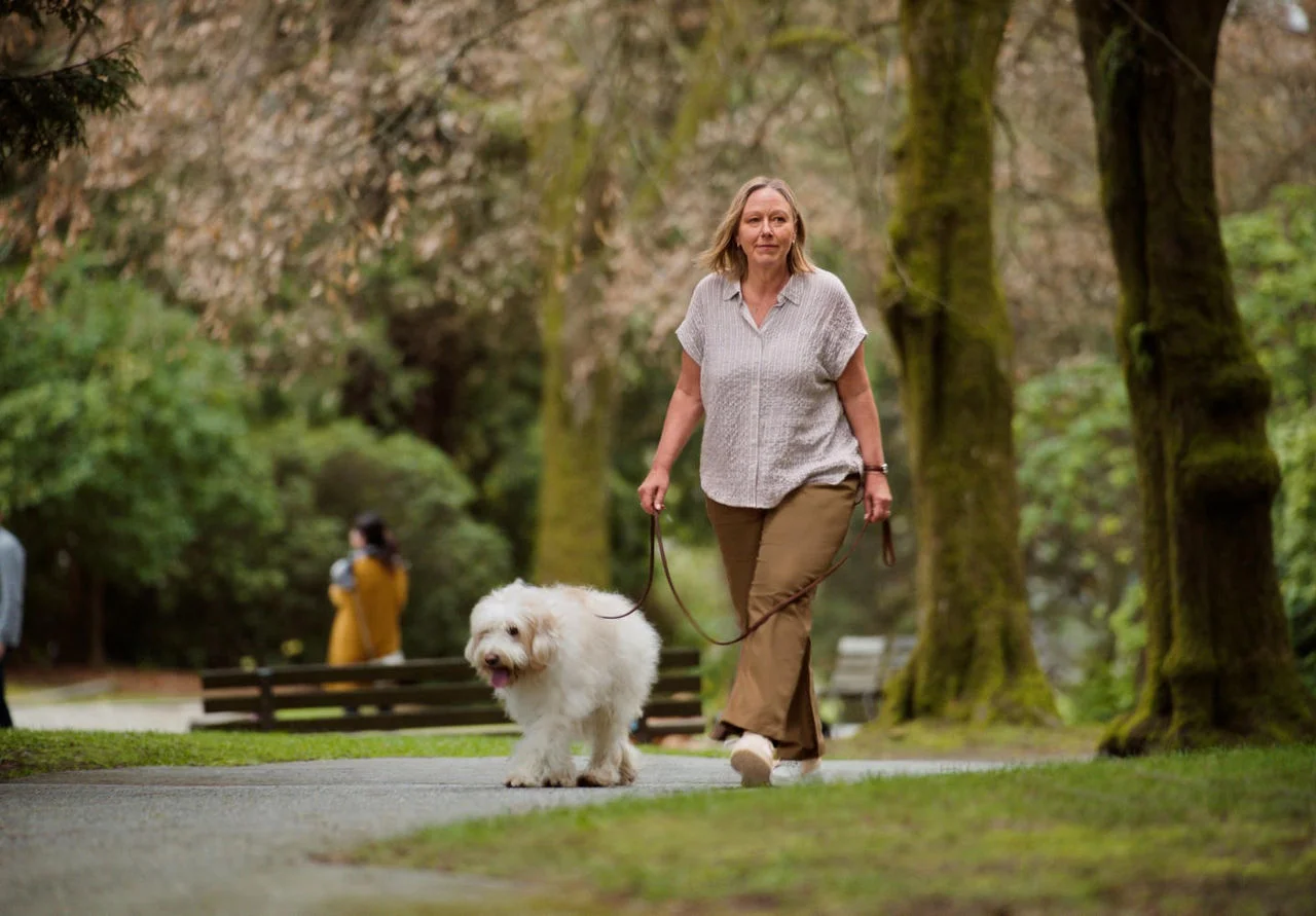 Senhora andando com cachorro em um parque arborizado