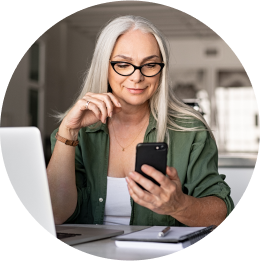 Woman looking at her smartphone as she sits at a desk in front of a computer