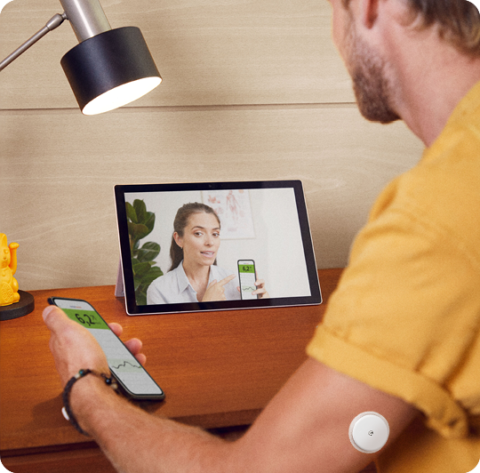 Muž so senzorom hovorí cez videohovor so svojou lekárkou, obaja majú v ruke smartfón s otvorenou aplikáciou FreeStyle LibreLink.