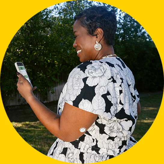 Woman smiling looking at a phone and wearing a FreeStyle Libre 3 Plus sensor