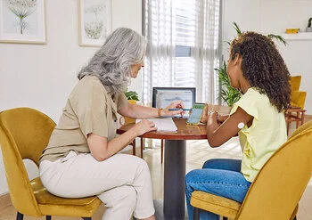 Senhora ensinando uma jovem sobre o aplicativo FreeStyle LibreLink. Ao fundo notasse uma tela com a pataforma Libre View