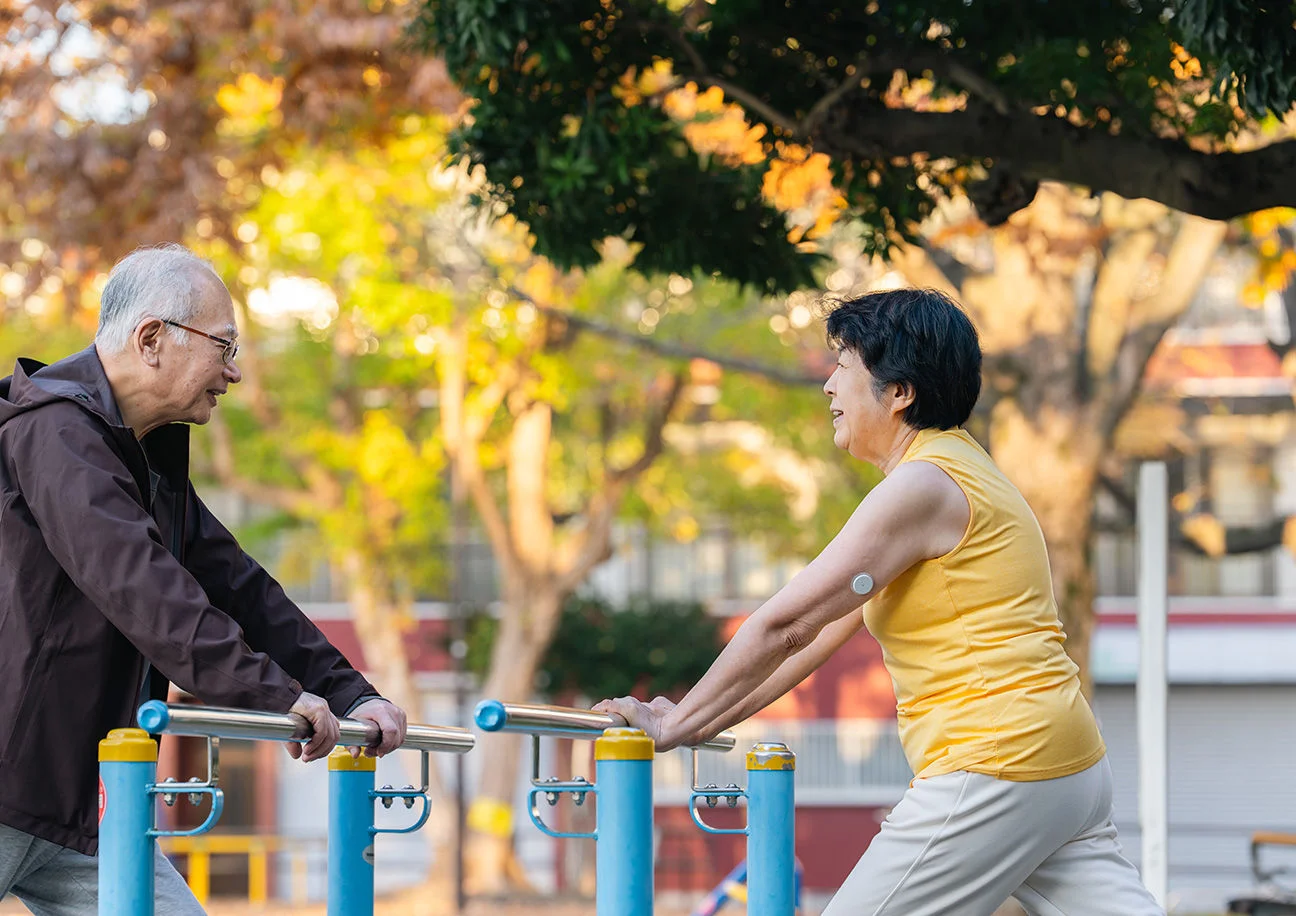 A woman wearing a sensor excercising in the park with her husband