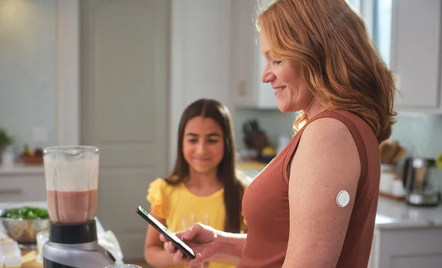 Person checking their glucose levels on their phone while making a smoothie with their child.