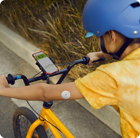 A kid riding his bike with a smartphone clipped to the handlebars with LibreLinkUp opened.