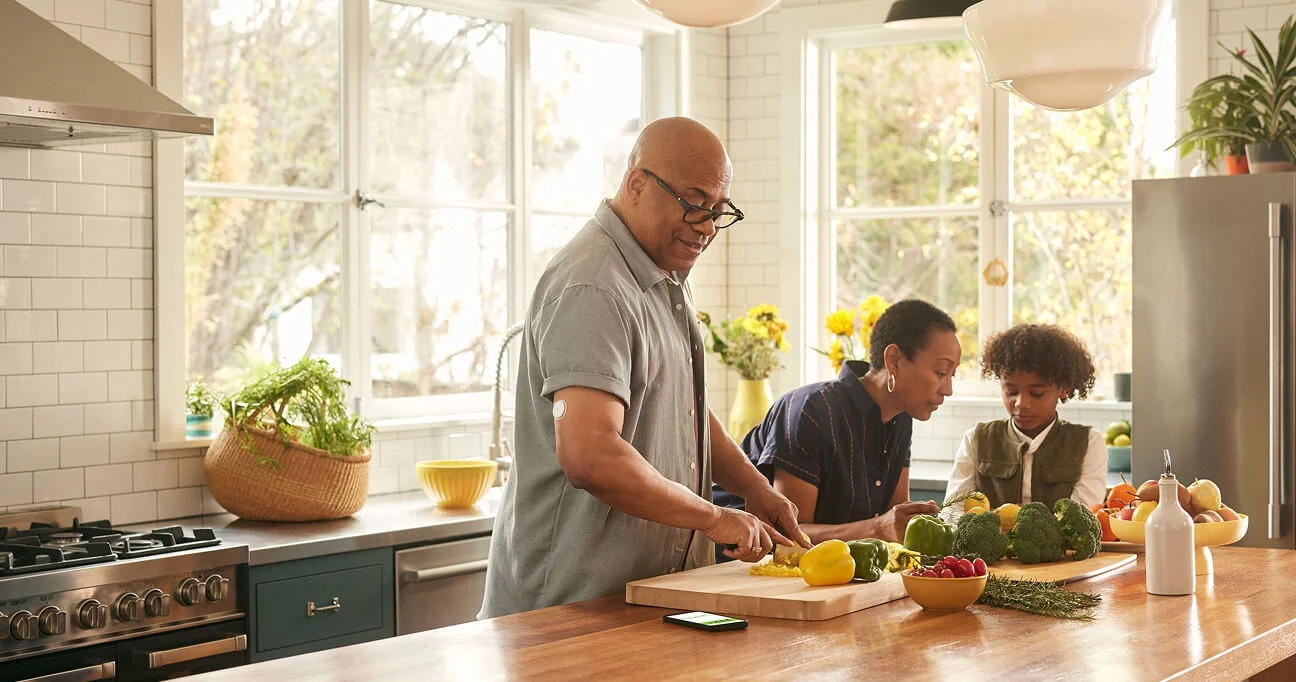 Hombre cocinando junto a su familia mientras usa el sensor FreeStyle Libre