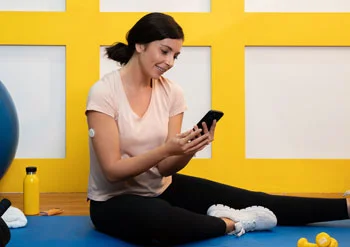 امرأة ترتدي مستشعر FreeStyle Libre وتجلس على الأرض وتنظر إلى شاشة هاتفها المحمول