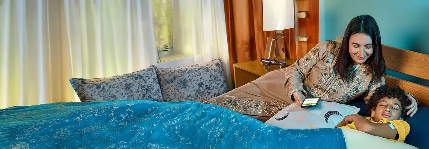 A woman sitting next to her son in the bed. The boy is wearing a freestyle libre sensor.