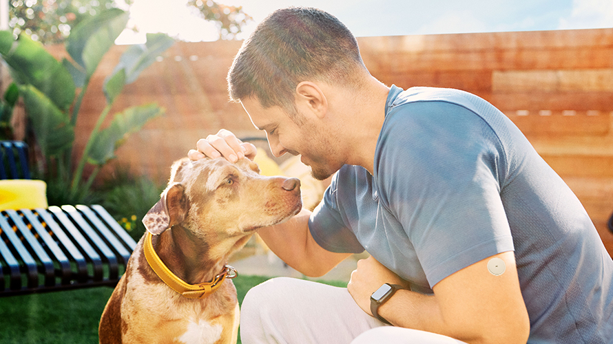 Homem com um sensor FreeStyle Libre no quintal fazendo carinho em um cachorro em um dia ensolarado