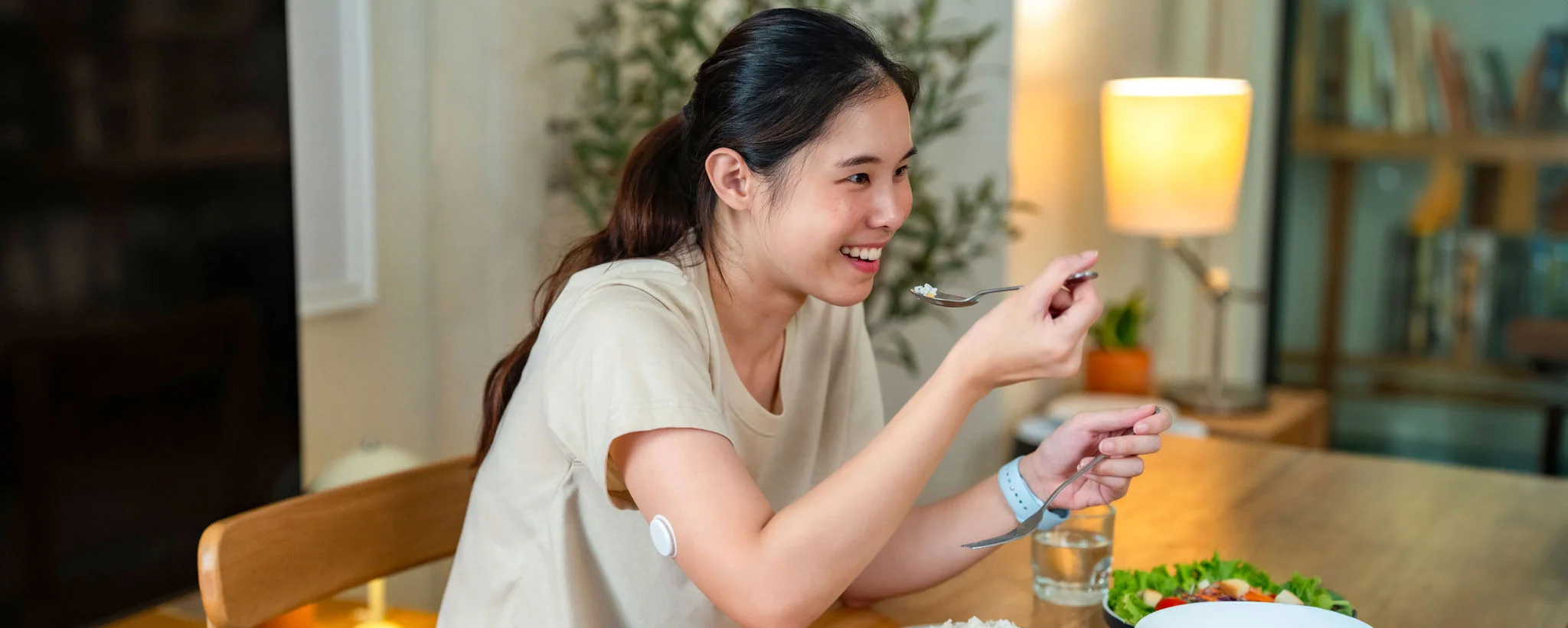A woman wearing a FreeStyle Libre sensor on the upper arm enjoys a meal at home while sitting at a table with food in front of them.