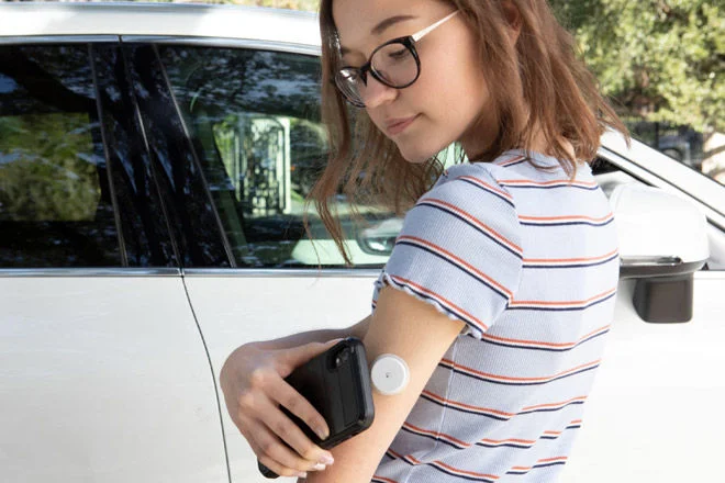 Menina com um sensor FreeStyle Libre em seu braço, fazendo o scan com seu smartphone