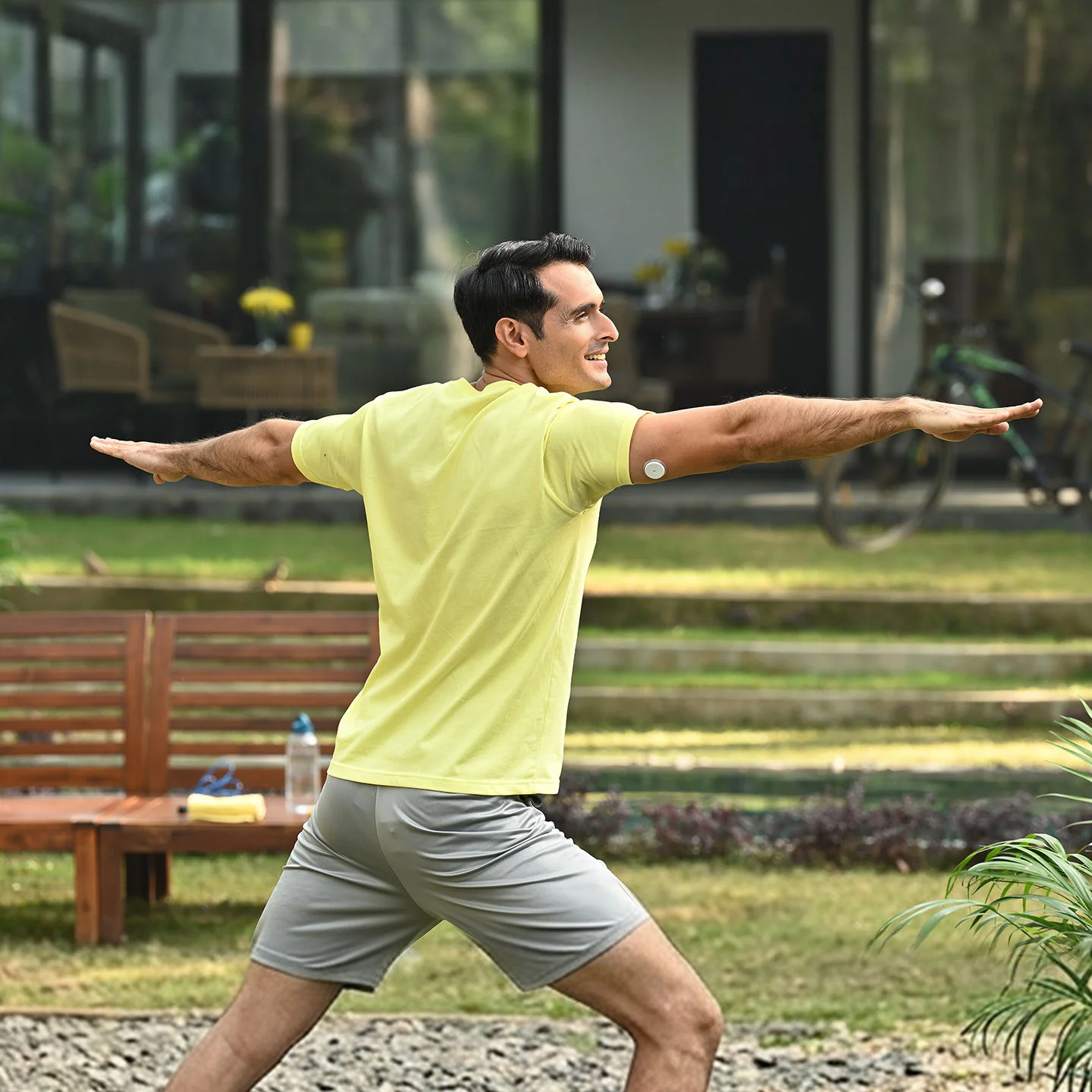 Man in a yellow shirt stretching in a park with a sensor on his arm.
