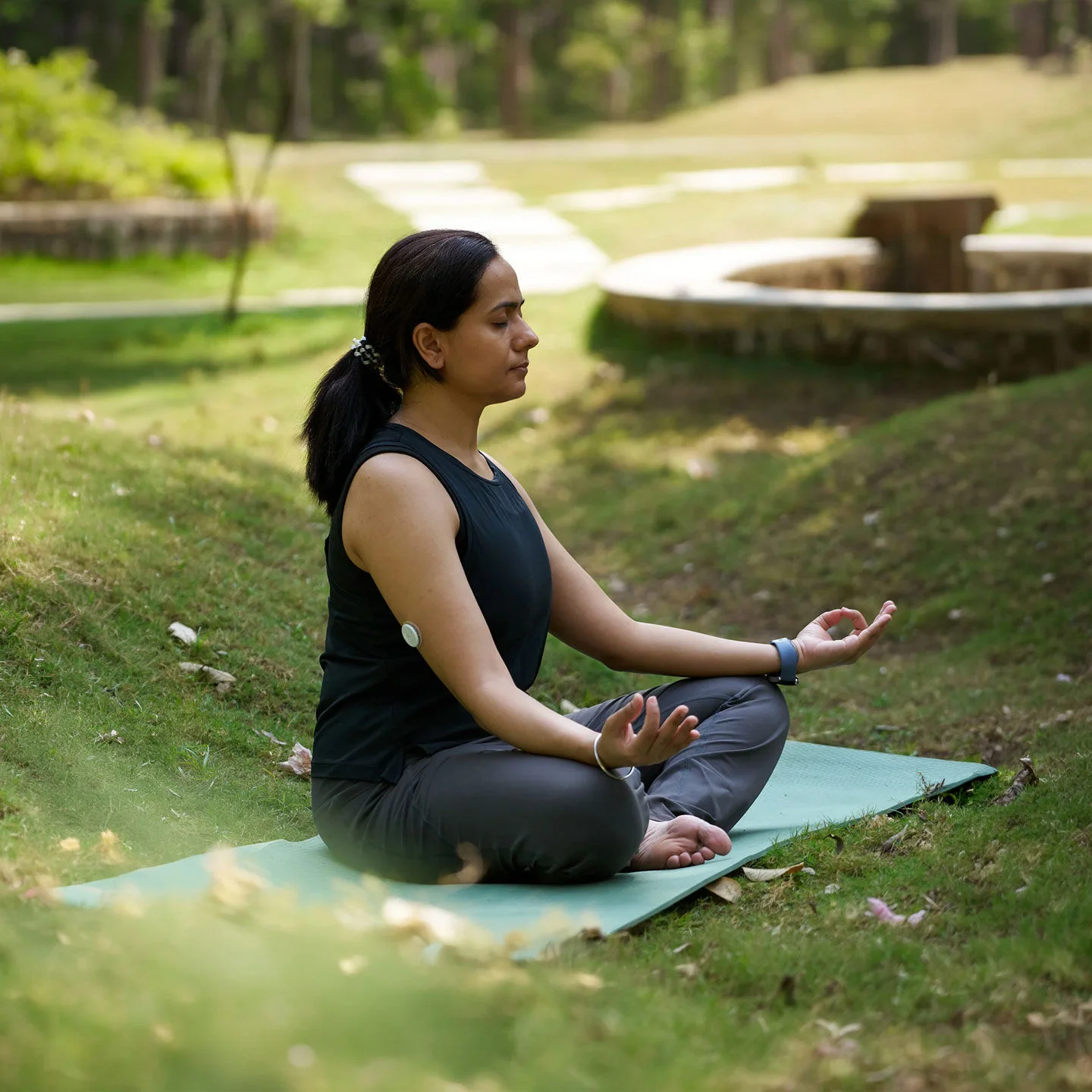 A woman meditating on a yoga mat with a glucose sensor on her arm.