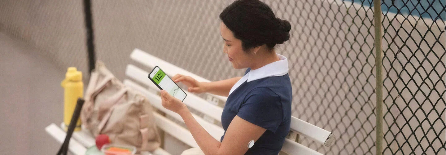 Pessoa sentada em um banco numa quadra de tênis, segurando um smartphone