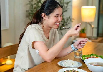 .A woman wearing a FreeStyle Libre sensor enjoys a healthy meal at home.