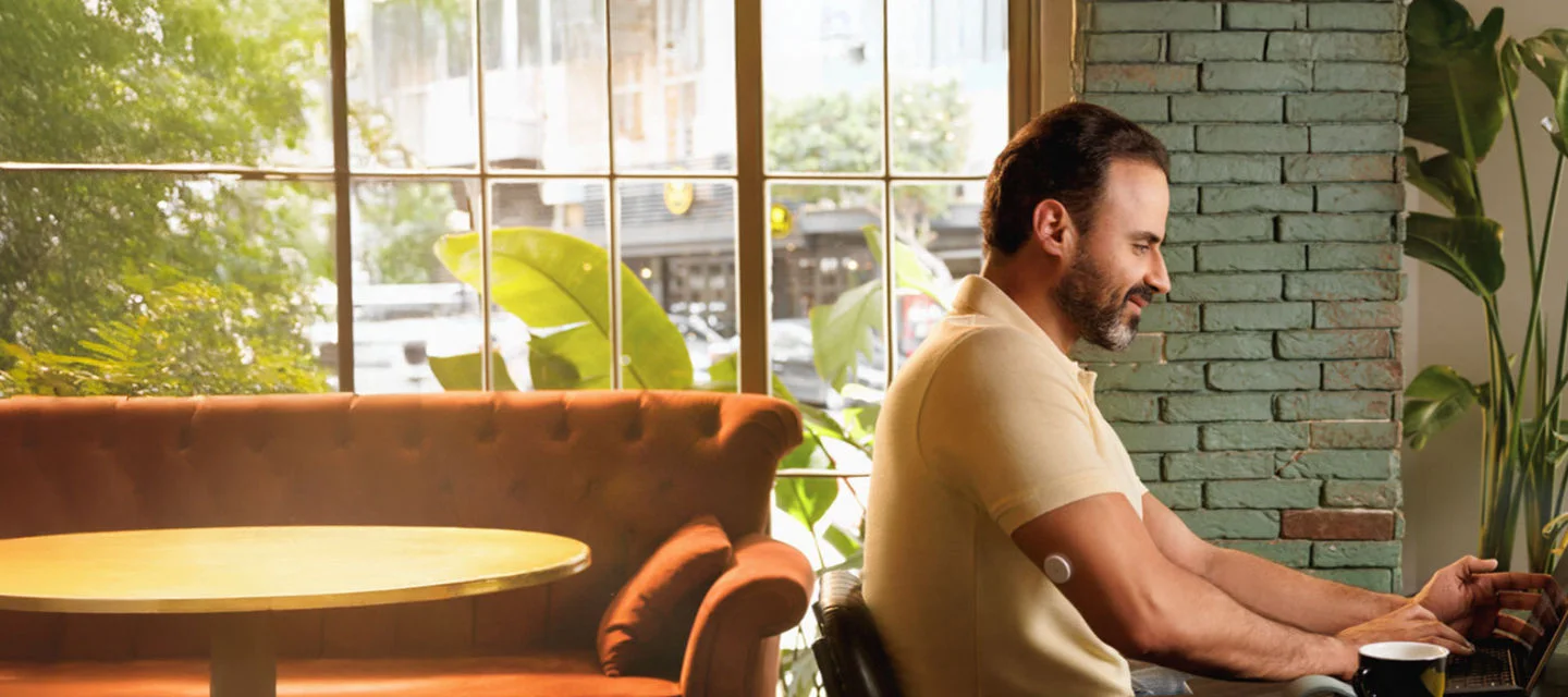 A man wearing a FreeStyle Libre sensor while sitting on a table using his laptop.