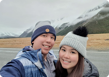 A couple standing outdoors in winter clothing with mountains behind them and a yellow butterfly icon beside the image.
