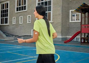 A woman wearing a FreeStyle Libre sensor, sitting on the floor, and clicking on her mobile.